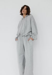 Szara bluza z kapturem i pasujące spodnie dresowe wykonane z miękkiej tkaniny. Luźny krój z elastycznymi ściągaczami w talii, na mankietach oraz z zamkiem błyskawicznym z przodu. Casualowy design.