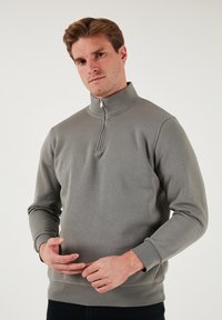 Felpa grigia con zip e colletto alto, realizzata in tessuto morbido. Presenta maniche lunghe e polsini a coste. Design semplice senza motivi.