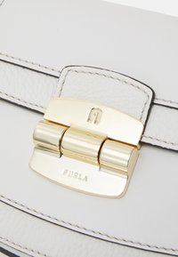 Sac à main en cuir délicat blanc avec une finition texturée. Comprend un fermoir et des accessoires en ton doré, un logo embossé et des coutures noires contrastantes.