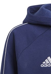 Sudadera con capucha azul marino de tela texturizada, con costuras decorativas blancas y un logo de Adidas bordado en la parte frontal izquierda.