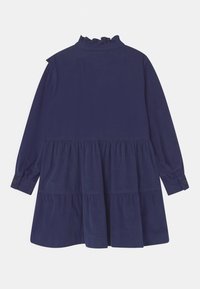 Granatowa sukienka z długimi rękawami, falbaną przy wysokim dekolcie oraz wielowarstwowym dołem. Wykonana z gładkiego materiału z akcentami zapinanymi na guziki przy mankietach.