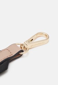 Guldmetallås med den ingraverade texten "VALENTINO" fäst vid ett band med läderdetaljer i beige och svart.