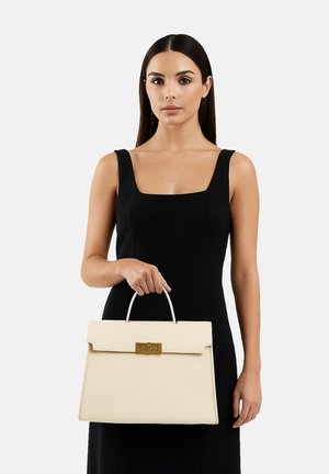 Sac à main en cuir crème avec une forme rectangulaire structurée, une poignée supérieure et des accents en métal doré. Le modèle porte une robe noire, se tenant devant un fond blanc.
