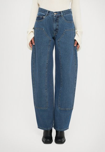 Blauwe wijde denim jeans met grote voorzakken, gedragen met zwarte vierkante laarzen en een crèmekleurige ribgebreide trui.