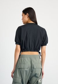 Black cropped top with puffed sleeves and drawstring at the waist, paired with green cargo pants featuring back pockets and elastic waistband.