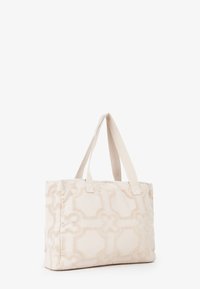 Sac fourre-tout en tissu beige avec un motif floral texturé, de forme rectangulaire, doté de deux poignées en tissu, sans quincaillerie ni accents visibles.