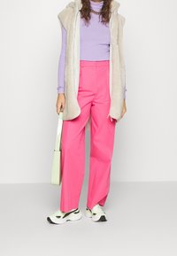 Pantalones anchos rosa, blusa de canalé morado claro, chaleco de piel sintética beige, bolso verde y zapatillas blancas con detalles negros.