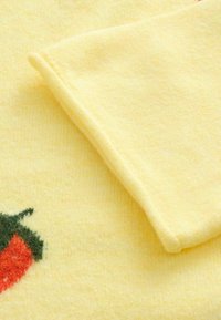 Tissu jaune doux avec un coin plié et un petit piment rouge brodé avec une tige verte en bas à gauche.