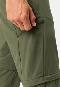 Pantaloni da escursionismo verdi con tasca con zip, realizzati in tessuto leggero e texturizzato. Logo VAUDE visibile sul lato sinistro.