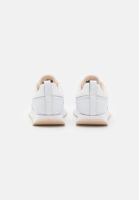 Sneakers in pelle bianca con un design minimalista, caratterizzati da una suola beige chiaro e dettagli beige. La vista posteriore mostra un pannello posteriore testurizzato.