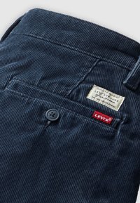 Pantalon Levi's en velours côtelé bleu foncé avec une poche arrière boutonnée, une étiquette blanche Levi Strauss et une étiquette rouge avec le logo Levi's.