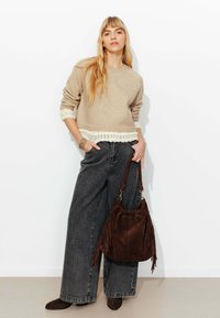 Pull beige en maille avec bordure en dentelle, associé à un jean large gris foncé. Accessoirisé avec un sac à franges en suède marron et des bottines.