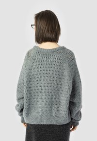 Pārmērīga pel�ēka adīta džemperis ar teksturētu rakstu, ribota apakšmalu un platām piedurknēm. Brīva piegriezuma dizains, kas piemērots slāņošanai.
