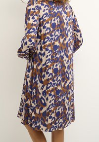 Vestito con stampa leopardata in tonalità beige, marrone e blu. Caratterizzato da maniche a sbuffo e un design ampio che arriva al ginocchio. Tessuto liscio e leggero.