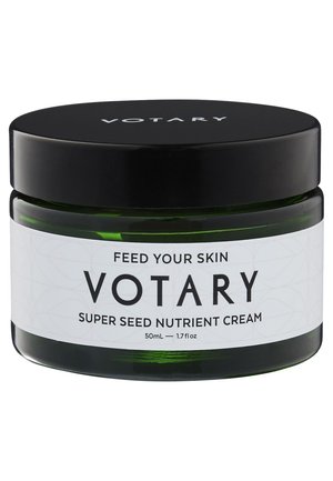 Jar en verre vert avec un couvercle noir à vis. Étiquette blanche avec du texte noir : "Crème nutritive Super Seed Votary, 50 mL." Texture lisse, design simple.