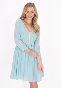 Rochie bleu deschis cu decolteu în V, mâneci lungi și fustă evazată. Are un accent roz la decolteu și talie, din material texturat.
