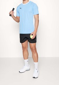 Camiseta atlética azul claro con detalles en blanco, pantalones cortos negros, calcetas blancas y zapatillas blancas. Sostenido una raqueta de tenis y una pelota verde.