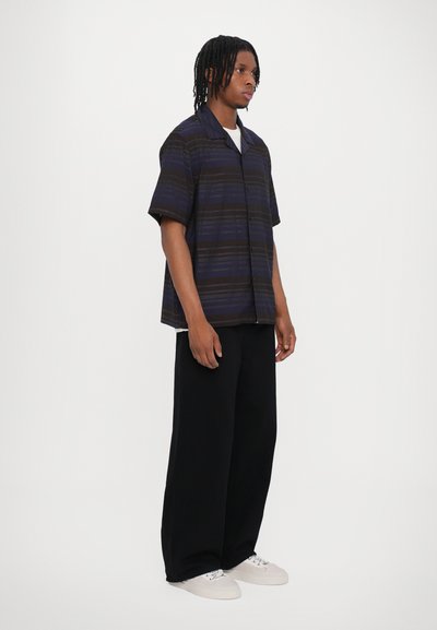 Chemise à manches courtes, boutonnée, en tissu rayé bleu marine et noir. Associée à un pantalon noir large et des baskets blanches. Coupe décontractée.