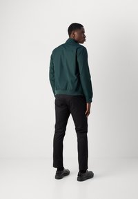 Grønn lettvektsjakke med krage, tilpasset design, elastisk hem, kombinert med svarte slim-fit bukser og svarte sko. Minimalistisk stil.