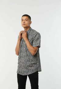 Korte mouw button-up shirt in zwart met wit bloemenpatroon. Beschikt over een spreidkraag en een rechte zoom, gemaakt van lichte stof.