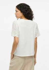 Camiseta de algodón blanca de manga corta con un ribete de encaje texturizado y con volantes en las mangas. Corte relajado; diseño liso en la parte posterior.