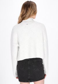 Witte, gestructureerde trui met een hoge kraag en een oversized pasvorm. Gecombineerd met een zwarte denimrok, met achterzakken.