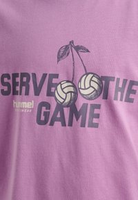 Lila Baumwoll-T-Shirt mit dem Aufdruck "Serve the Game" in dunkler Schrift, begleitet von einer Grafik mit zwei Volleyballs und Kirschblättern.