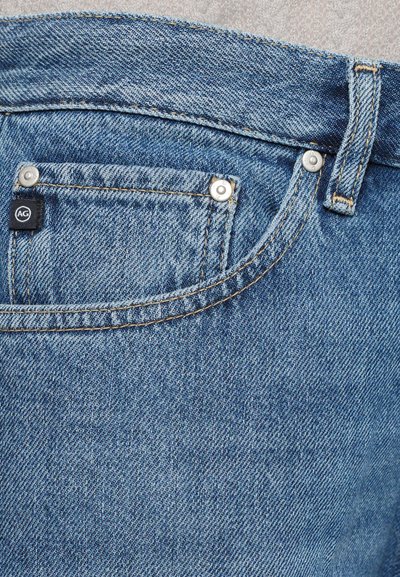 Gai zila denim bikses ar priekšējo kabatu, sudraba detaļām un mazu melnu etiķeti. Iespējama redzama šuvju struktūra un nedaudz valkāta tekstūra.