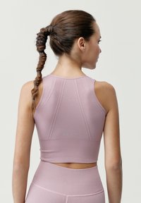 Svetloružový športový crop top s hladkou textúrou, ktorý má pretekársky strih a vertikálne švy.