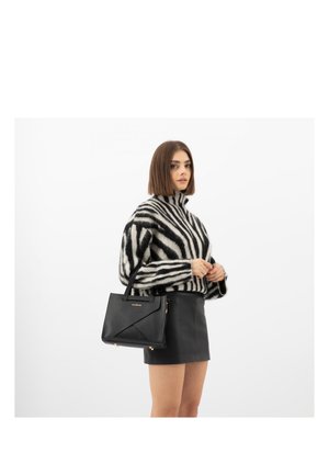 Kobieta w czarno-białym golfie w paski i czarnej skórzanej mini spódniczce, trzymająca czarną torebkę ze złotymi detalami.