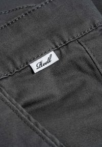 Grauer Stoff mit glatter Textur, der sichtbare Nähte und ein weißes Etikett aufweist, das in die Naht eingenäht ist und den Namen "Reell" zeigt.