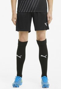 Sorte fodboldshorts og sorte knælange sokker med hvide Puma-logoer; lyseblå fodboldstøvler med et farverigt mønster.