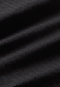 Crna tkanina s suptilnom herringbone teksturom, koja se odlikuje glatkim nabranim dijelovima i mekanim završetkom. Nema vidljivih uzoraka ili metalnih dijelova.