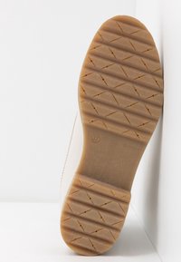Suela de zapato con un fondo de goma texturizado y con patrón en marrón claro, con una parte superior lisa en beige. Talla 37 marcada en la suela.