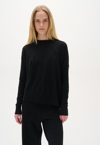 Schwarzer Pullover mit langen Ärmeln, entspannter Passform, weicher Textur und geradem Saum. Kombiniert mit passenden schwarzen Hosen, minimalistisches Design.