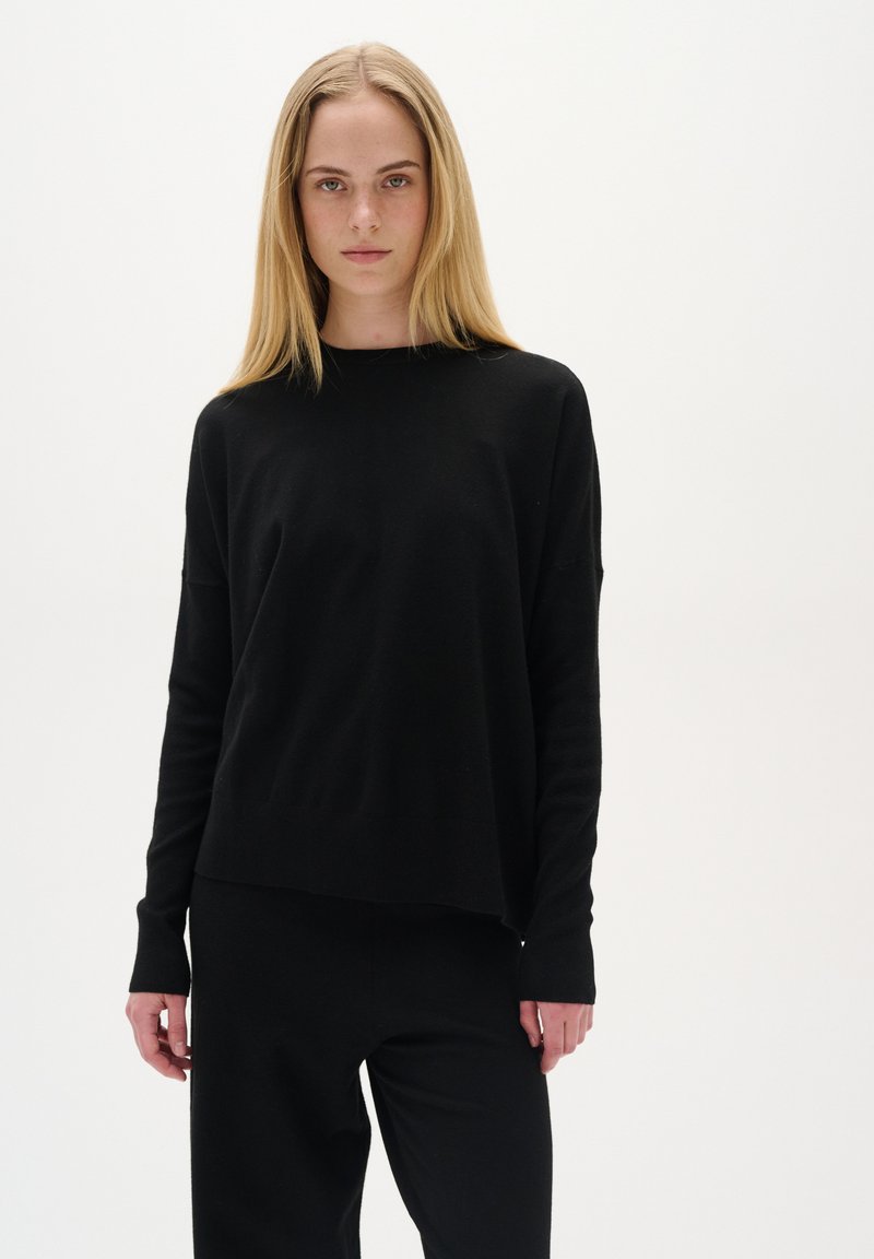 Schwarzer Pullover mit langen Ärmeln, entspannter Passform, weicher Textur und geradem Saum. Kombiniert mit passenden schwarzen Hosen, minimalistisches Design.
