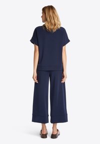 Top blu navy di taglio ampio con maniche corte, abbinato a pantaloni a gamba larga. Il tessuto sembra morbido, con una texture liscia e dettagli minimi.