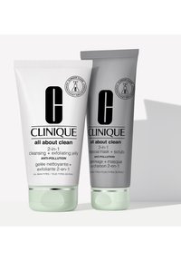 Ensemble "Tout sur la propreté" de Clinique : deux tubes, un blanc et un gris, avec des accents vert menthe. Présente un branding clair et des descriptions de produit.