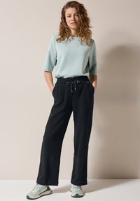 Haut bleu clair à manches courtes associé à un pantalon large noir texturé avec une taille à cordon et des accents blancs ; présenté avec des baskets.