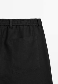 Pantaloni corti neri in lino con vita elastica e una tasca posteriore singola con cuciture pulite. Il tessuto presenta una leggera texture.