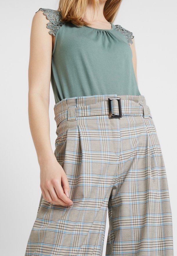 Grön ärmlös topp med spetsdetaljer; vida rutiga byxor i beige, blå och brun med bälte i midjan och pressesvik fram.