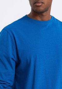 Sininen pitkähihainen t-paita, joka on valmistettu pehmeästä kankaasta; siinä on pyöreä kaula-aukko ja sileä pinta. Ei näkyviä kuvioita tai metalleja.