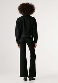 Crna traper jakna s napuhanih ramena, uparena s crnim trapericama na zvono. Materijal je čvrst, s detaljima šavova i stražnjom oznakom. Crne čizme na petu.