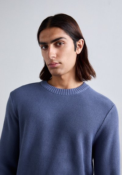 Blå strikket sweater med en struktureret overflade, der har en rund halsudskæring og ribbede kanter. Designet inkluderer tætsiddende ærmer og en afslappet pasform.