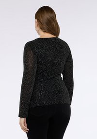 Schwarzes Langarmoberteil mit strukturierter Oberfläche, verziert mit silbernen Punkten. Es zeichnet sich durch eine taillierte Passform, einen runden Ausschnitt und eine leichte Stretch-Qualität aus.