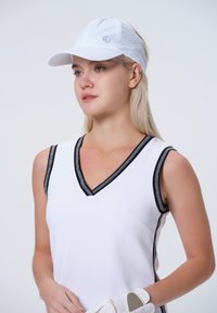 Biała bezrękawnik z dekoltem w serek, zdobiony czarnymi wykończeniami i przeszyciami. Biała czapka z logo oraz biała rękawiczka dopełniają sportowy look.