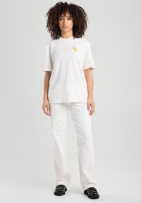 White short-sleeve t-shirt featuring a small lemon graphic, paired with white flared pants and black shoes. Smooth fabric texture.