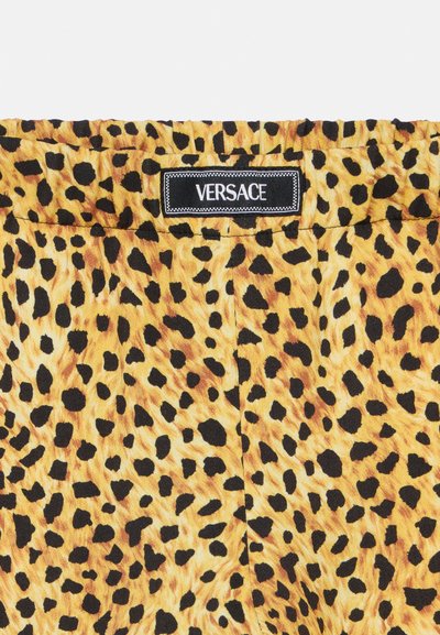 Ύφασμα με μοτίβο λεοπάρδαλης σε αποχρώσεις του κίτρινου και του μαύρου, με ετικέτα Versace με έντονα γράμματα σε ομαλή υφή.