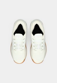 Een paar witte sportschoenen met een mesh textuur, witte veters en tan kleuren zolen, van bovenaf weergegeven op een lichtgrijze achtergrond.