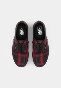 Zapatillas de lona en cuadros rojos y negros con cordones y suela negra. Presentan un logo de Vans en la plantilla. Diseño clásico de corte bajo.